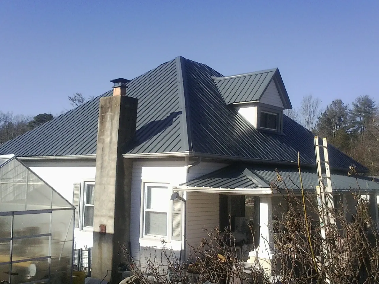 Dark blue standing seam metal roof on a white farmhouse with dormer — Slate & Tile Roof Repair by Roofing Brothers in Oak Creek