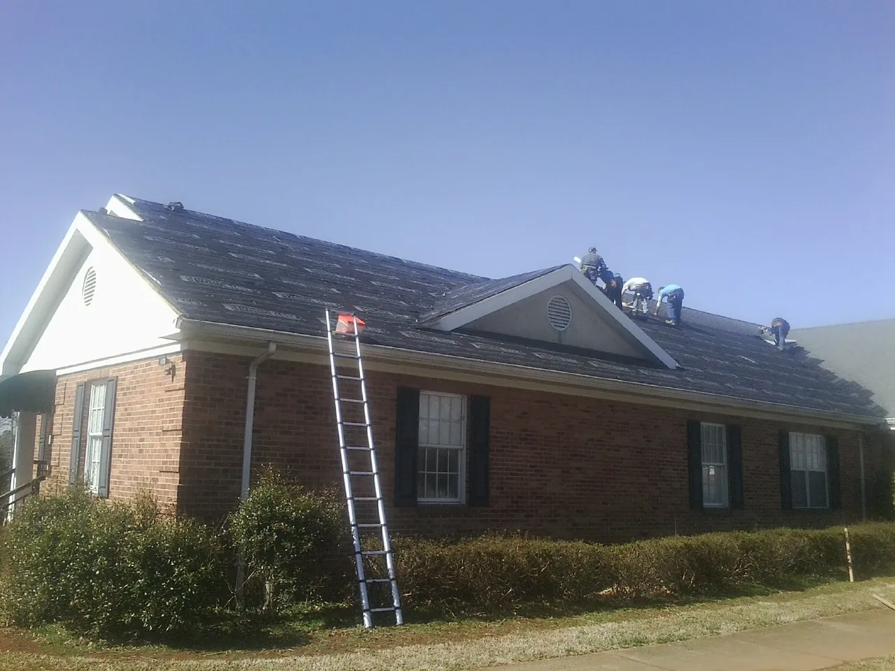 Crew tearing shingles off a brick ranch roof with a ladder set — Metal Roof Repair work by our crew in Oak Creek