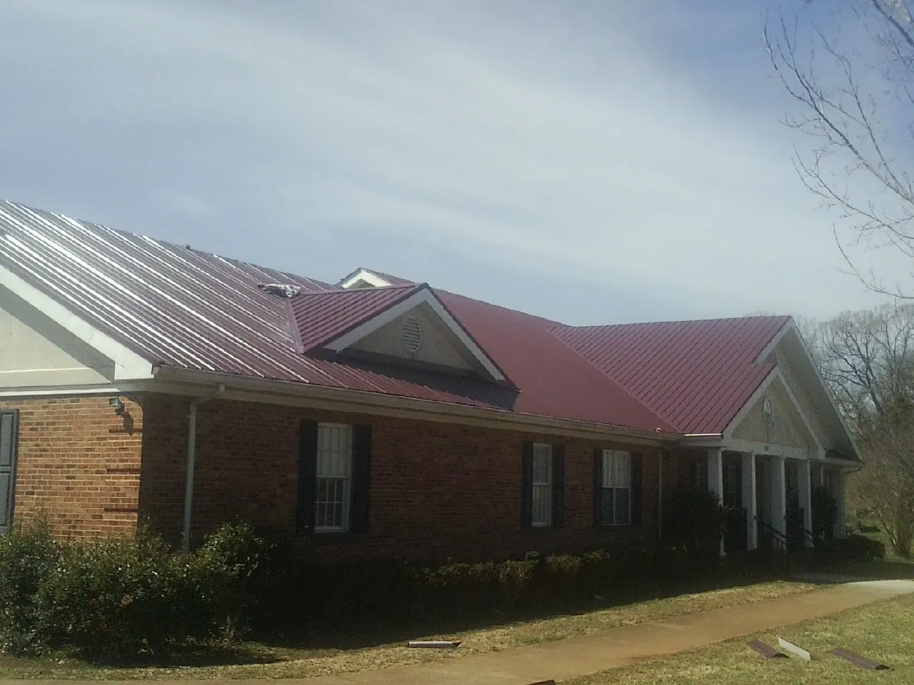 Red metal roof with gabled entries on a long brick building, from a Hail Damage Roof Repair job in Oak Creek