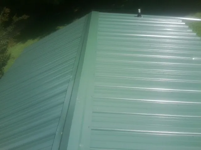 New green metal panels meeting at the ridge of a roof — Flat Roof Repair work by our crew in Oak Creek