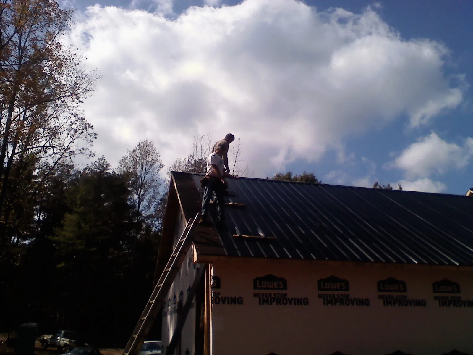 Roofer fastening dark metal panels high against a cloudy sky, from a Roof Inspection job in Oak Creek