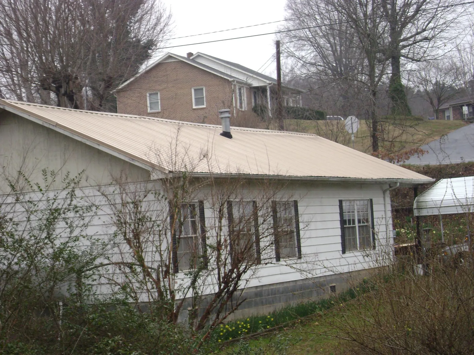 Tan metal roof on a white sided house set into a hillside — Commercial Roofing by Roofing Brothers in Oak Creek