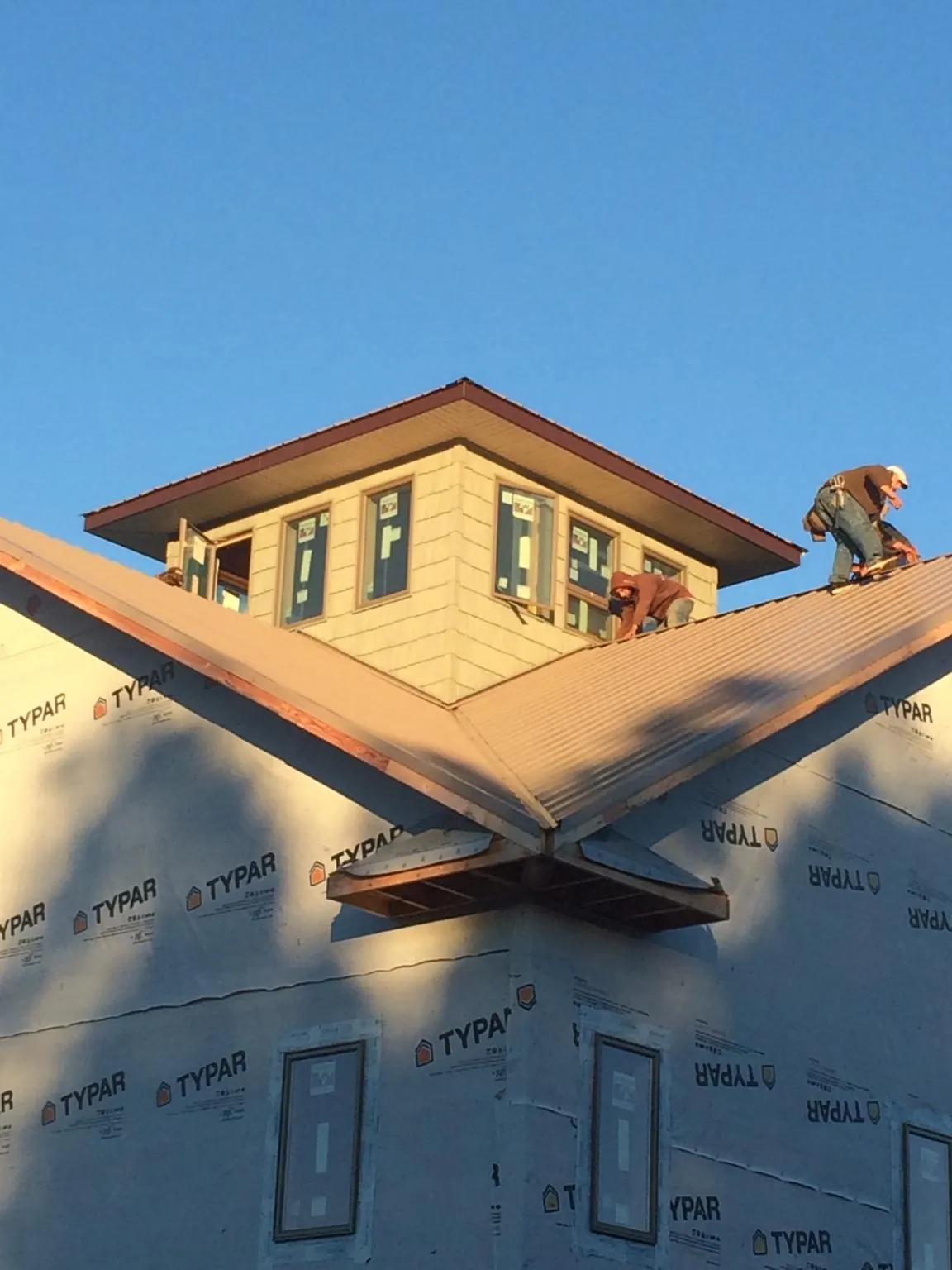 Roofers working around a rooftop cupola on a new metal roof at sunset — Roof Waterproofing in Oak Creek by Roofing Brothers